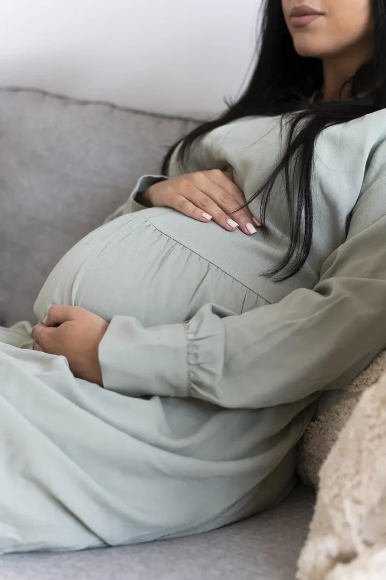 Close-up of a pregnant woman sitting on a couch, cradling her belly with a serene expression - Dream IVF Cyprus, Comfort and Support Throughout Your Pregnancy Journey